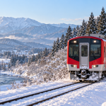 Red and white train traveling through a snowy mountain landscape in Japan